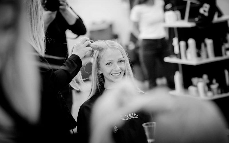 Smiling woman having her hair styled in a salon setting, captured in black and white.