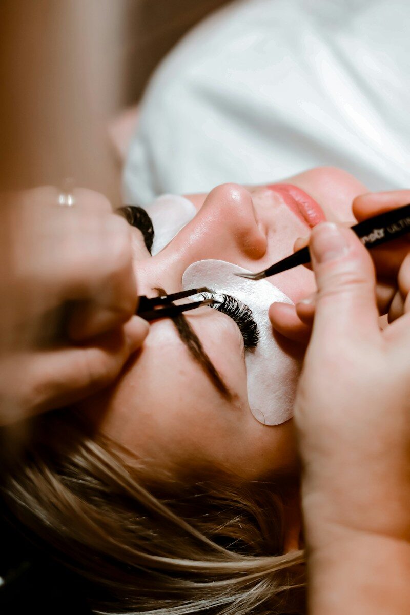 A person applying eyelash extensions to a client with tweezers in a salon
